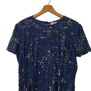 May include: A navy blue sequined dress with a short sleeve and a round neckline. The dress is covered in a floral pattern with silver sequins.