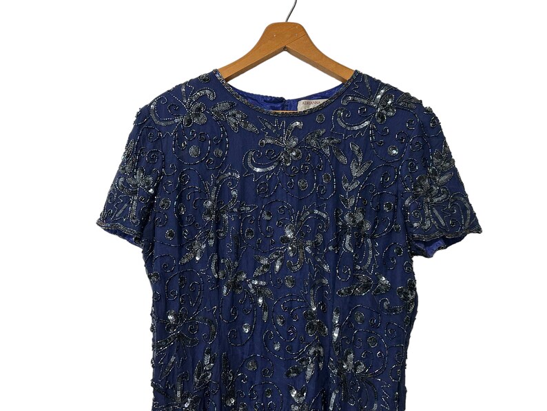 May include: A navy blue sequined dress with a short sleeve and a round neckline. The dress is covered in a floral pattern with silver sequins.