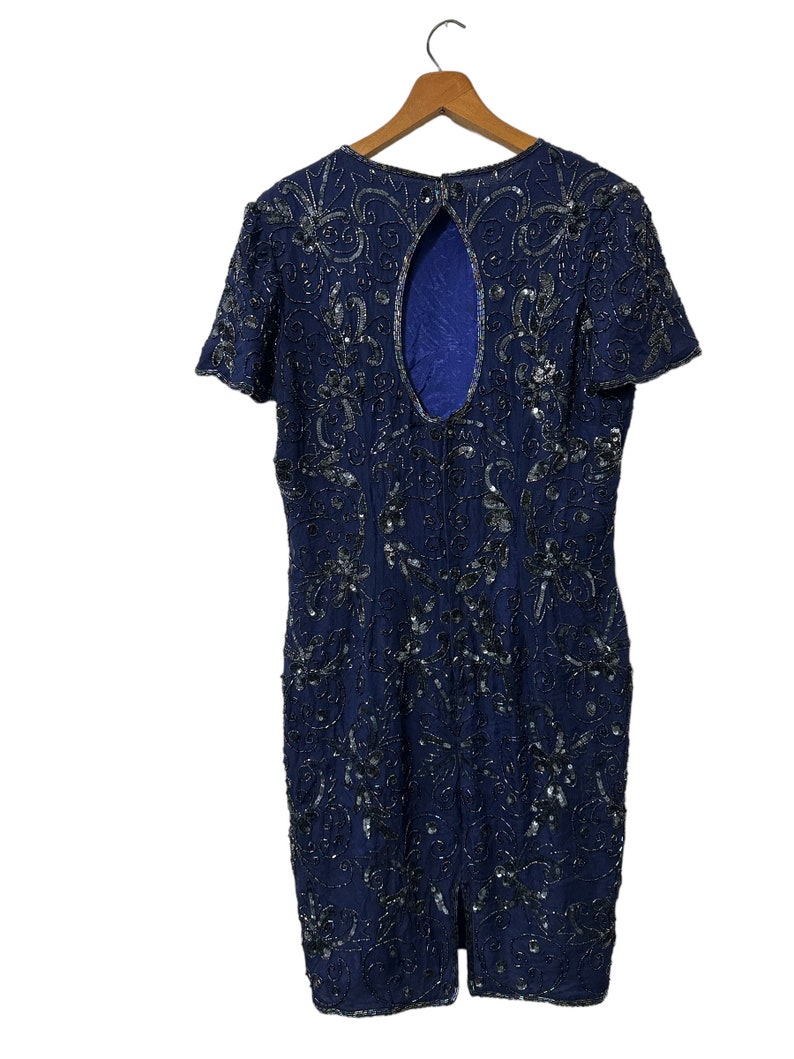 May include: A navy blue sequined dress with a keyhole back and short sleeves. The dress is fully covered in silver sequins in a floral pattern.