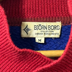 K&ouml;nnte beinhalten: Roter, blauer und brauner Strickpullover mit einem Bj&ouml;rn Borg-Etikett. Das Etikett lautet "Collection Design Rohdi Heintz" und "M".