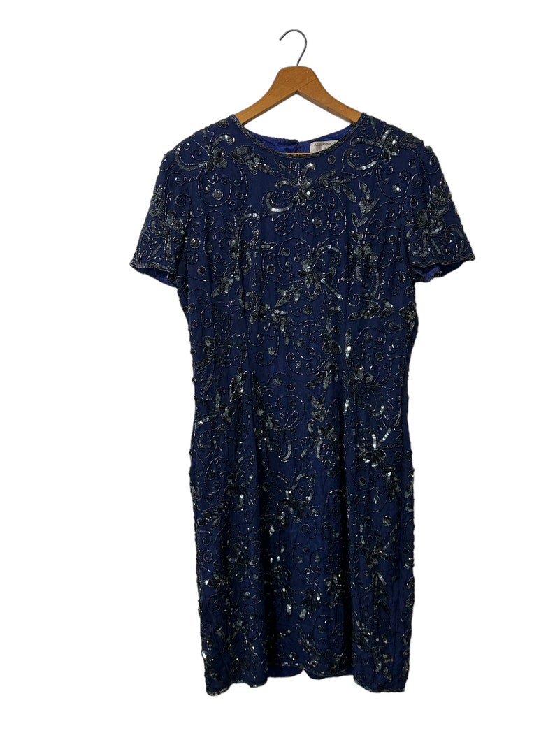 May include: A navy blue sequined dress with a short sleeve and a round neckline. The dress is covered in silver sequins in a floral pattern.