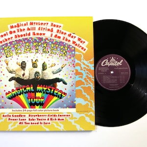 Può includere: Un disco in vinile e la sua copertina gialla per l'album Magical Mystery Tour dei Beatles. La copertina presenta una grafica colorata con i membri della band in costume, un arcobaleno e i titoli delle canzoni come Hello Goodbye.