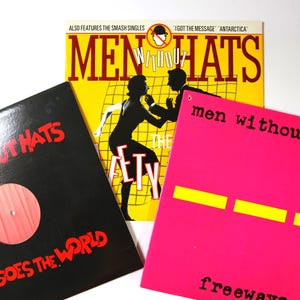 May include: Three vinyl record sleeves by Men Without Hats. One is yellow with a black silhouette of two people, one is black with red text reading Pop Goes The World, and one is bright pink with black text reading men without hats freeways.