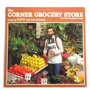 May include: Vintage album cover for "The Corner Grocery Store" by Raffi. The cover features a man in an apron holding tomatoes, surrounded by produce and plants. The album title and artist's name are prominently displayed.