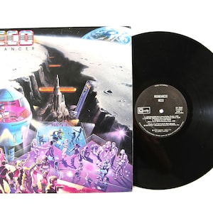 May include: A Meco Moondancer vinyl record and its square cardboard album cover. The cover features a space-themed illustration with a futuristic dome, a lunar landscape, and people dancing on a purple platform. The black vinyl record shows a central label.