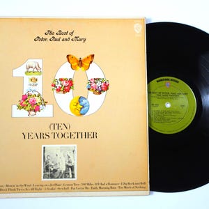 Op de afbeelding: Vintage vinylalbum getiteld "The Best of Peter, Paul and Mary". De bruin-beige albumhoes toont het nummer 10 versierd met illustraties. Een zwarte vinylplaat is zichtbaar naast de albumhoes.