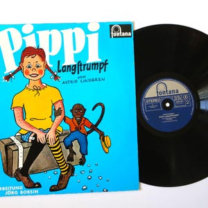 May include: A vintage vinyl record and album cover for "Pippi Langstrumpf" by Astrid Lindgren. The album cover is bright blue with a cartoon illustration of Pippi Longstocking and a monkey. The record is black.
