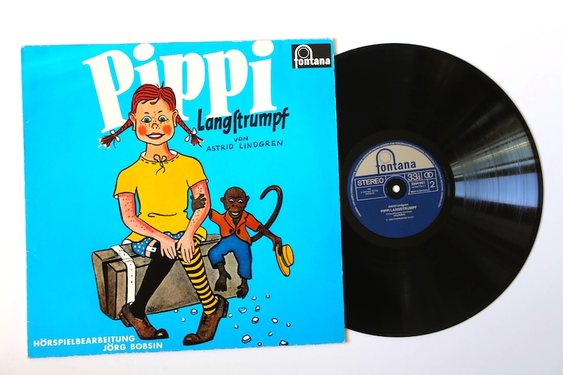 May include: A vintage vinyl record and album cover for "Pippi Langstrumpf" by Astrid Lindgren. The album cover is bright blue with a cartoon illustration of Pippi Longstocking and a monkey. The record is black.