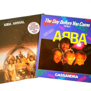 May include: Two ABBA album covers. The "Arrival" album cover shows the band in front of a helicopter. The "The Day Before You Came" single cover is blue with the band's faces and the song title. Both are vintage records.