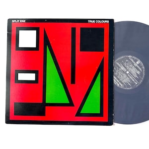 May include: A Split Enz "True Colours" vinyl record album. The album cover features a bold design with a red background, black geometric shapes, and a green triangle. The album title and band name are visible.