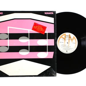 May include: A black vinyl record and its square cardboard sleeve. The sleeve features the text Split Enz and Waiata, with a pink and black graphic of musical notes. A red rectangular sticker lists song titles. The record has a white center label.