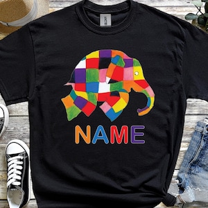 May include: Black t-shirt with a vibrant, patchwork-style elephant design. The word "NAME" is printed in rainbow colours beneath the elephant. The t-shirt has a crew neck.