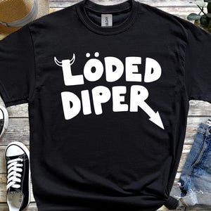 May include: Black crew neck t-shirt with the white text "LÖDED DIPER" and a white arrow. The shirt is displayed with black and white trainers and a straw hat. The t-shirt is made of cotton.