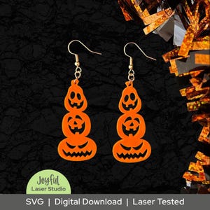 May include: A pair of orange Halloween earrings shaped like stacked jack-o'-lanterns. Each earring features three carved pumpkin faces with gold-colored ear wires. The earrings are a digital download from Joyful Laser Studio.