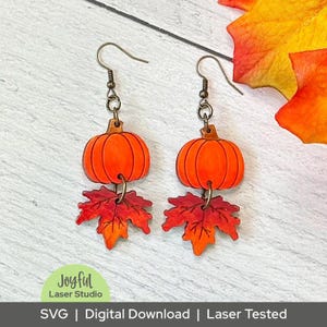 May include: A pair of fall-themed earrings featuring orange pumpkin pendants with brown stems and red and orange maple leaf charms. The earrings are suspended from bronze-colored ear wires. The image includes the text "Joyful Laser Studio" and "SVG | Digital Download | Laser Tested".