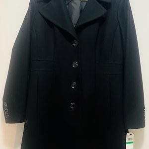 May include: A black Anne Klein coat with a classic design. The coat features a notched collar, four buttons down the front, and buttons on the sleeves. The coat is hanging on a wooden hanger.