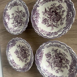 Puede incluir: Cuatro cuencos de cerámica antiguos con un diseño floral y de pájaros en tonos morados y blancos. Los cuencos tienen un borde festoneado y están dispuestos sobre una superficie de madera. Los cuencos varían en tamaño y son adecuados para servir.