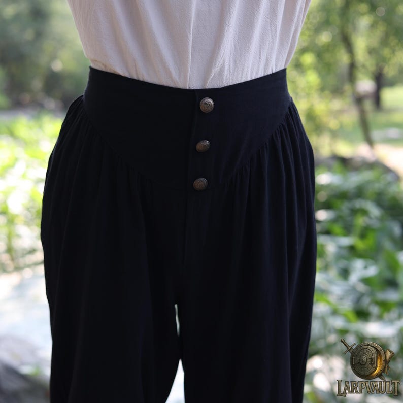 May include: Black high-waisted pants with three decorative buttons. The pants have a wide waistband and a loose, flowing fit. The pants are made of a soft, dark fabric and are suitable for historical reenactment or costume events.
