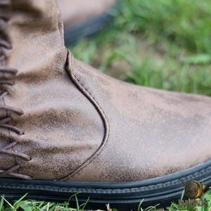 Puede incluir: Bota de cuero marr&oacute;n con cordones y acabado envejecido. La bota tiene una suela negra y est&aacute; sobre hierba verde. El dise&ntilde;o sugiere una est&eacute;tica vintage o r&uacute;stica.