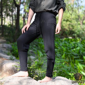 May include: Black pants with a drawstring waist and lace-up detail on the lower leg. The pants are made of a soft material and are suitable for historical reenactments or cosplay.