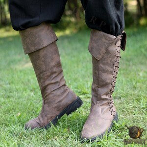 Puede incluir: Botas marrones hasta la rodilla con acabado texturizado y suelas negras. Las botas tienen un pu&ntilde;o doblado y un dise&ntilde;o de cordones en la parte trasera. Hechas de material similar al cuero, son adecuadas para cosplay o disfraces.