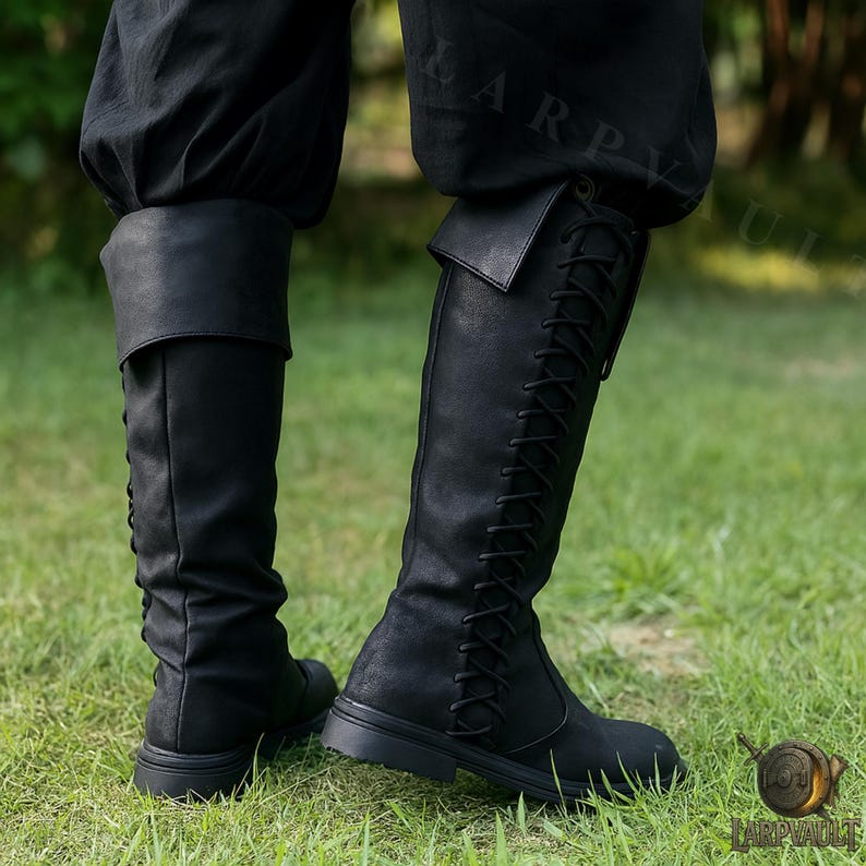 Puede incluir: Botas negras hasta la rodilla con dise&ntilde;o de cordones y pu&ntilde;o doblado. Las botas son de material texturizado y tienen suela plana. Se usan con pantalones negros y sobre un fondo de hierba verde.
