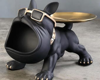 Könnte beinhalten: Schwarze Bulldoggen-Figur mit goldenen Akzenten. Die Bulldogge trägt eine goldgerahmte Sonnenbrille und ein goldenes Halsband. Sie hat ein goldenes Tablett auf dem Rücken und ein offenes Maul zur Aufbewahrung.