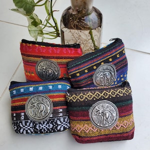 May include: Four small, colorful coin purses with zipper closures. Each purse features a woven fabric design in red, blue, black, and yellow, and a silver-colored elephant emblem. The purses are arranged together, showcasing their unique patterns.
