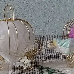 May include: Four decorative pumpkin-shaped carriages made of thin gold wire. Each carriage features a central sphere in orange, white, purple, or filled with seashells. The carriages have small gold wire wheels and decorative accents like white snowflakes.