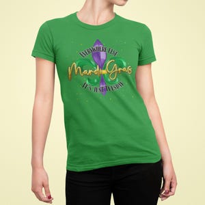 May include: A green t-shirt featuring a gold-colored "Mardi Gras" script and a purple fleur-de-lis design. The text "Everywhere Else It's Just Tuesday" is above and below the script. The shirt is worn by a person.