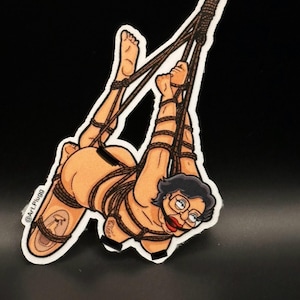 Peut inclure: Un autocollant représentant une illustration de dessin animé d'une personne attachée avec une corde. La personne a les cheveux noirs courts, des lunettes et du rouge à lèvres rouge. L'autocollant a une bordure blanche.