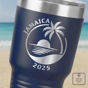 May include: A navy blue insulated travel mug with a silver lid. The mug has a white graphic of a palm tree, sun, and ocean scene with the word "JAMAICA" and the year "2025" in a circular design.
