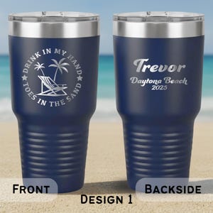 May include: Navy blue insulated travel mug with a silver rim and lid. The front displays a beach scene with text: "DRINK IN MY HAND, TOES IN THE SAND." The back has the name "Trevor" and "Daytona Beach 2025."