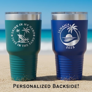 May include: Two insulated tumblers with silver lids. One is teal with the text "DRINK IN MY HAND TOES IN THE SAND" and a beach scene. The other is blue with "JAMAICA" and a palm tree design. Both have a sand-like design at the bottom.