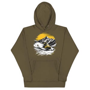 Puede incluir: Sudadera con capucha verde oliva con un diseño gráfico de una moto de nieve en un paisaje montañoso nevado, con un sol amarillo. El diseño es circular. La sudadera tiene una capucha con cordón y un bolsillo delantero.