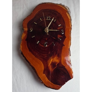 May include: A wall clock crafted from a polished, irregular wood slice featuring a dark reddish-brown center and lighter amber edges. The clock face displays gold-colored numerals at 3, 6, 9, and 12, with matching gold-colored hour, minute, and second hands.