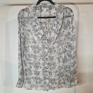 May include: A sheer, button-down blouse with a large collar. The shirt features a white and gray floral pattern over a plaid background. The brand name "Pendleton" is visible on the collar.