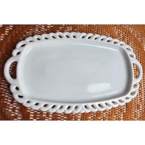 May include: A white ceramic serving tray with a smooth, glossy finish and an oval shape. The tray features a decorative lattice-style border with an openwork pattern and two integrated handles on the sides for easy carrying and handling.