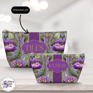 Puede incluir: Dos neceseres con cremallera con un diseño floral en tonos morados, verdes y dorados. La bolsa más grande tiene la palabra "TILES" y la más pequeña la palabra "EXTRAS". Las bolsas están sobre una superficie de madera clara.