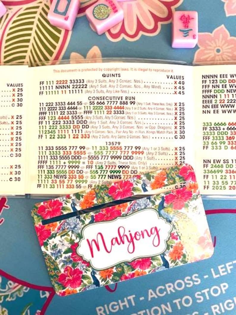 Pu&ograve; includere: Un colorato porta carte Mahjong con un design floreale e la parola "Mahjong" in corsivo. Il porta carte &egrave; decorato con fiori rossi, uccelli blu e foglie verdi. Sono visibili tessere di Mahjong rosa.