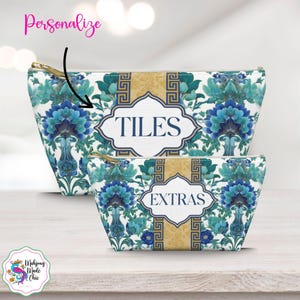 Op de afbeelding: Twee make-up tassen met ritssluiting met een bloemenpatroon in blauw en teal. De grotere tas heeft het woord "TILES" in een witte, sierlijke lijst, en de kleinere tas zegt "EXTRAS". Beide tassen hebben goudkleurige ritsen.