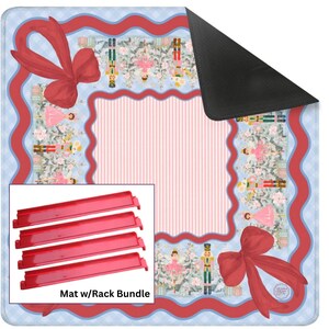 Pu&ograve; includere: Un tappetino quadrato con sfondo a quadretti azzurro, bordo ondulato rosso e grandi fiocchi rossi. Il centro presenta strisce verticali rosa, circondate da un motivo di schiaccianoci e ballerine. Include quattro rastrelliere rosse.
