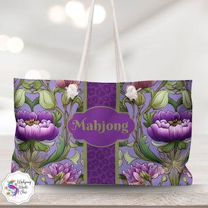 May include: A large tote bag with a floral design in shades of purple, green, and white. The bag features a central panel with the word "Mahjong" in a decorative font. The bag has white rope handles.
