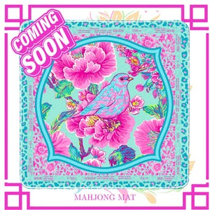 May include: A Mahjong mat with a vibrant design. It features a blue and pink bird amidst pink flowers, set within a turquoise frame. The mat is framed in pink, with the words "COMING SOON" and "MAHJONG MAT" displayed. The overall design is bright and eye-catching.