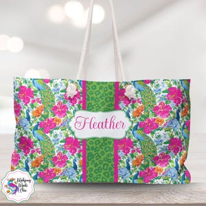 May include: A large tote bag with a vibrant floral and peacock feather pattern. The bag features a green leopard print stripe down the center with the name "Heather" in a white frame. White rope handles complete the design.