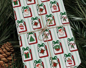 May include: Wrapped gift with Christmas-themed wrapping paper. The paper features a repeating pattern of gift boxes with Santa Claus, Christmas trees, and candy canes. The gift is tied with twine and set against a backdrop of pine needles and a pine cone.