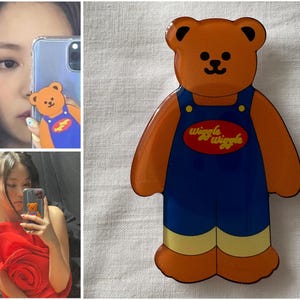May include: A brown bear-shaped phone case with blue dungarees and the text "wiggle wiggle". The case is shown in a mirror selfie with a person holding the phone.