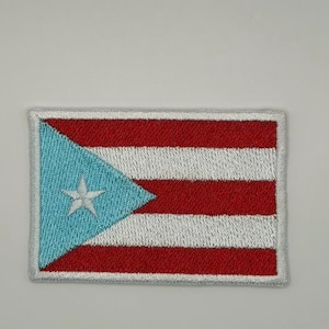 May include: A rectangular embroidered patch featuring the flag of Puerto Rico. The design consists of five horizontal stripes in alternating red and white, with a light blue triangle on the left side containing a single white five-pointed star.