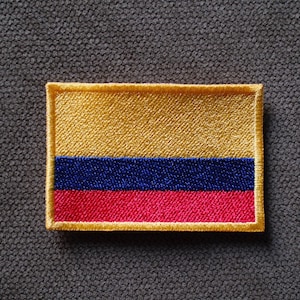 May include: A rectangular embroidered patch featuring the horizontal tricolor flag of Colombia. The design consists of a wide yellow band on top, a blue band in the middle, and a red band on the bottom, all bordered by a thick yellow stitched edge.