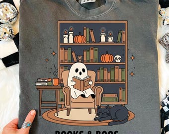 May include: Dark gray sweatshirt with a Halloween-themed graphic. The design features a ghost reading a book in a chair, a bookshelf with pumpkins and candles, and a black cat. The text "BOOKS & BOOS" is at the bottom.
